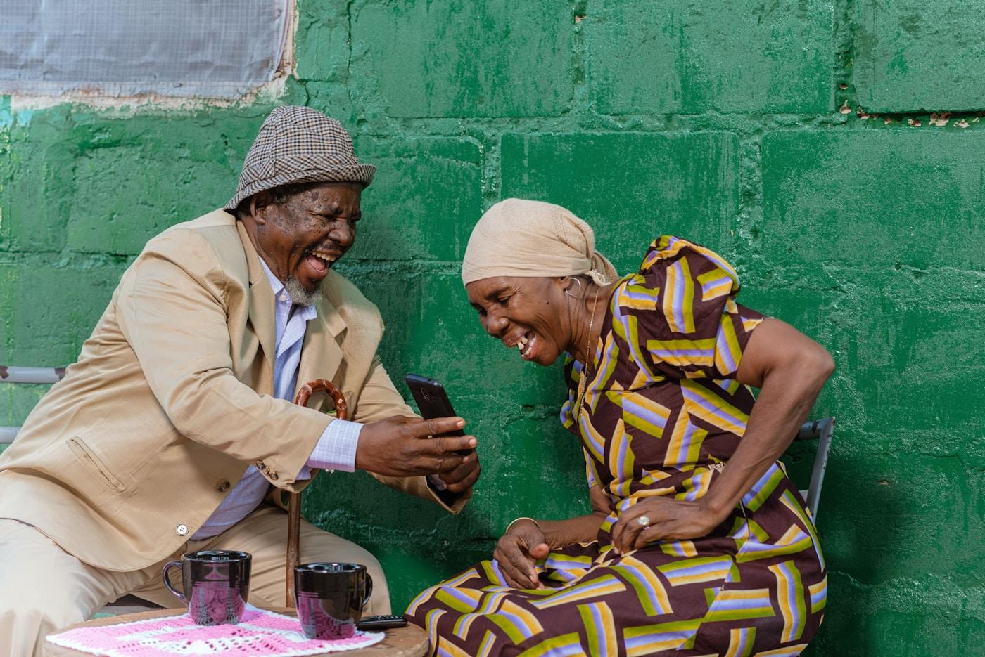 An older couple sitting on a bench laughing while looking at a phone together