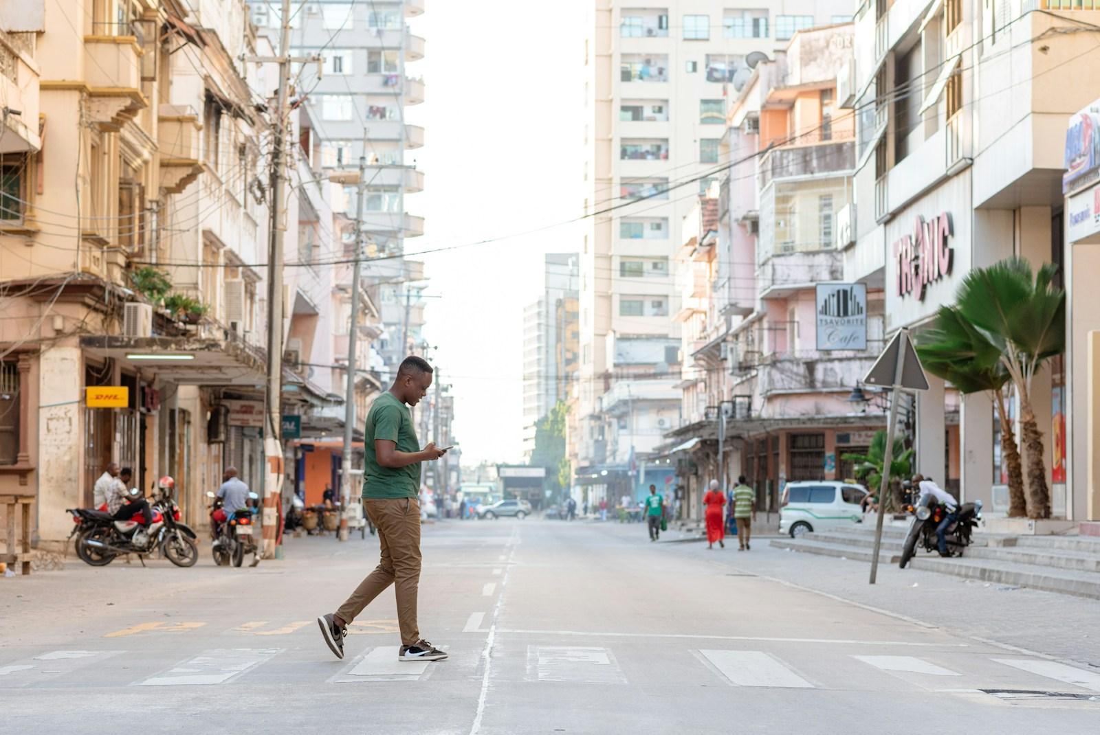 A man crossing a street in Dar es Salaam while reading a message on his phone